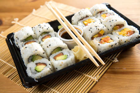 Salmon, avocado and mango inside California sushi with soy sauce, pickled ginger and wooden chopstick in take away Bento boxの写真素材