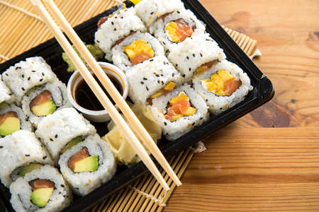 Salmon, avocado and mango inside California sushi with soy sauce, pickled ginger and wooden chopstick in take away Bento boxの写真素材