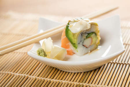 Surimi avocado rainbow inside sushi roll with salmon avocado topped with wasabi, pickled ginger and wooden chopsticksの写真素材