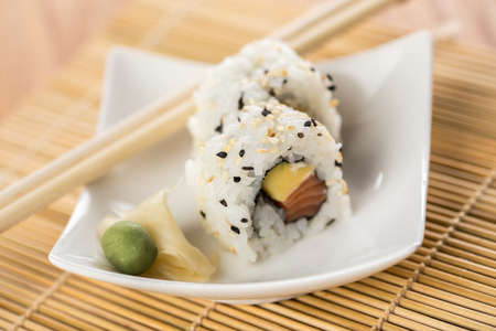 Two salmon mango inside out California sushi rolls with wasabi, pickled ginger and woodenの写真素材
