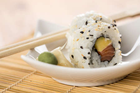 Two salmon mango inside out California sushi rolls with wasabi, pickled ginger and woodenの写真素材