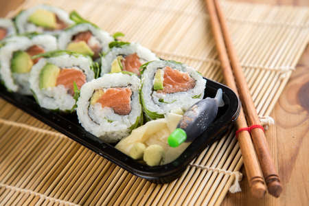 Salmon avocado rocks inside sushi with soy sauce, picking ginger and chopstick in take away trayの写真素材