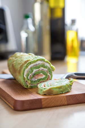 Spinach pancake with smoked salmon and cream cheese on wooden board in domestic kitchenの写真素材