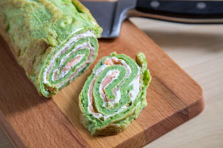 Spinach pancake with smoked salmon and cream cheese on wooden board in domestic kitchenの写真素材