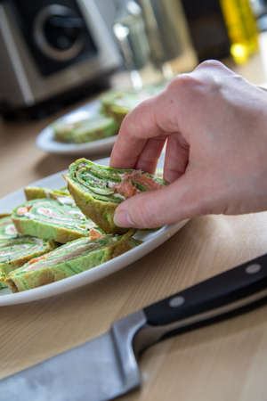 Woman cut and arrange spinach pancake roll with smoked salmon and cream cheese in domestic kitchenの写真素材