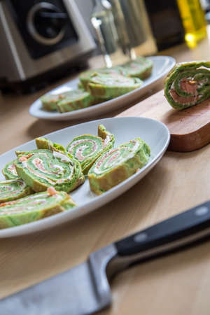 Arranged slices of spinach pancake roll with smoked salmon and cream on plate in domestic kitchenの写真素材
