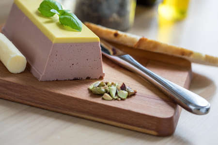 Belgian duck liver with champagne jelly, basil, butter, bread and pistachios on wooden board in domestic kitchenの写真素材
