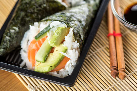 Two Japanese Temaki hand roll sushi with raw salmon, avocado and cucumber in a tray with soy sauceの写真素材