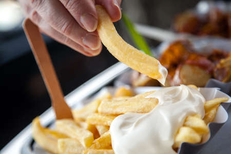 Man eating French fries with mayonnaise and German curry sausage with curry sauce on food marketの写真素材