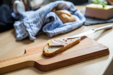 Slice of bread with gourmet Belgian duck liver and knife on wooden board in domestic kitchenの写真素材