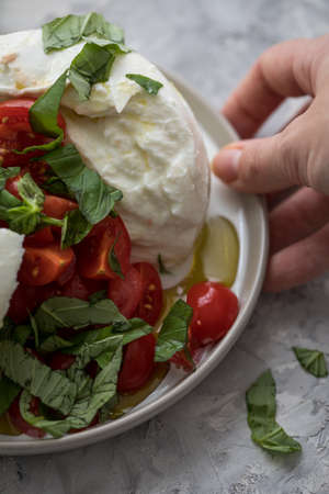 Woman having buffalo mozzarella cheese ball with tomatoes, basil, olive oil and white balsamic vinegar on plateの写真素材