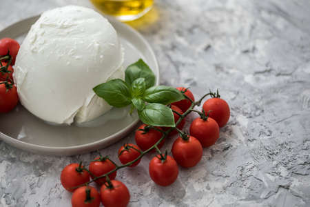 Buffalo mozzarella cheese ball with cocktail tomatoes, basil and olive oil on plateの写真素材