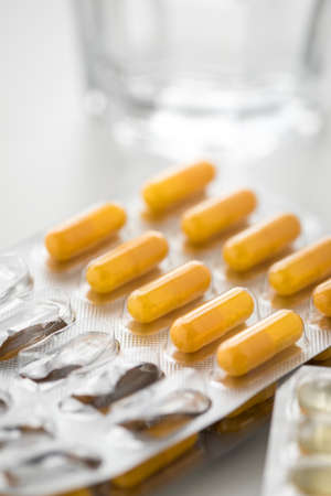 Two blister of yellow pills tablets medicine with glass of waterの写真素材
