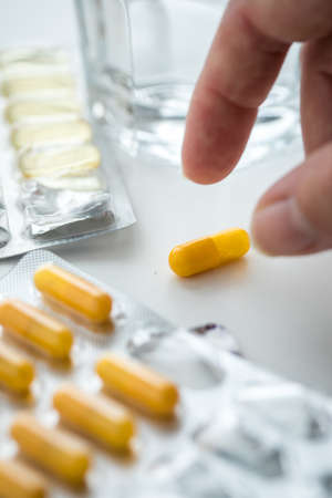Woman taking yellow pills tablets medicine of blister with glass of waterの写真素材