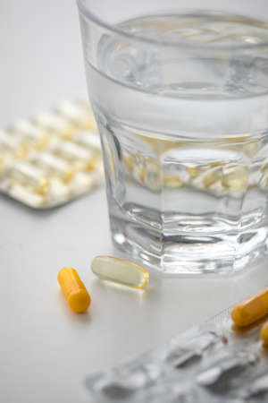 Two blister of yellow pills tablets medicine with glass of waterの写真素材