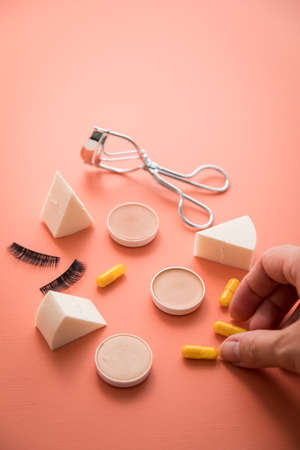 Woman taking beauty pills, camouflage, make-up sponge, false lashes and lash curler for styleの写真素材