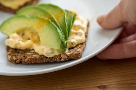 Woman eating avocado egg salad on sunflower seed whole grain bread slice with turmeric for breakfast or snackの写真素材
