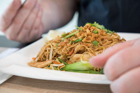 Man eating Chinese fried noodels with chicken, onions, coriander and Pak Choi in Restaurant