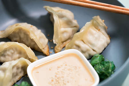 Fried Dim Sum Gyoza dumplings with Wakame seaweed salad and sesame sauce in bowl with wooden chopsticks for lunchの写真素材