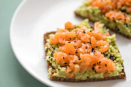 Avocado smoked salmon on sunflower seed whole grain bread slice with sesame seeds for breakfast or snack on mint green backgroundの写真素材