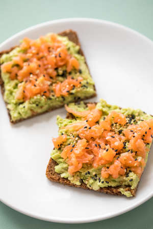 Avocado smoked salmon on sunflower seed whole grain bread slice with sesame seeds for breakfast or snack on mint green backgroundの写真素材