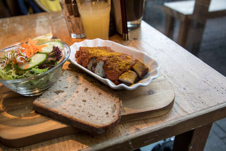German gourmet currywurst grilled and sliced sausage with curry ketchup, salad and slice of rustic bread on wooden board in restaurantの写真素材