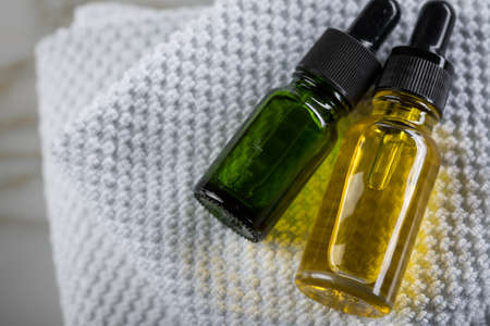 Two bottles of green natural serum and yellow organic beauty face oil for cosmetic anti age treatment skin care on towels and marble backgroundの写真素材