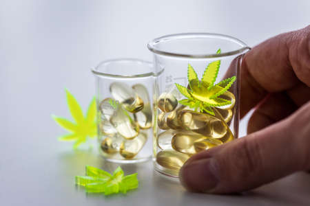 Woman using pills, tablets, capsules of cannabis marijuana hemp and CBD in lab scale glass beaker as...