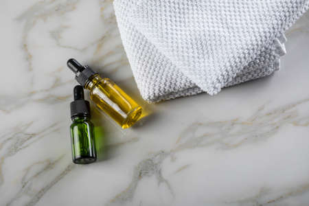 Two bottles of green natural serum and yellow organic beauty face oil for cosmetic anti age treatment skin care on towels and marble backgroundの写真素材