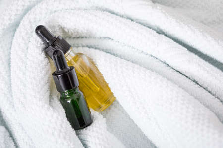 Two bottles of green natural serum and yellow organic beauty face oil for cosmetic anti age treatment skin care on towels and marble backgroundの写真素材