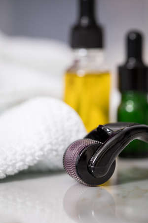 Derma roller, towel, yellow cosmetic oil  and green serum dropper bottles for anti ageing lifting or acne treatment on marble backgroundの写真素材