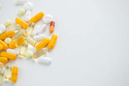 White and yellow pills, tablets and capsule medicine on white background