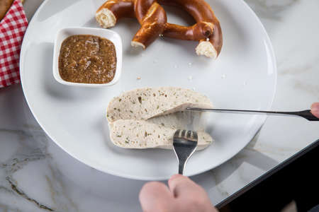 Man eats Munich white sausage with knife and fork, sweet mustard and pretzel and take off sausage...