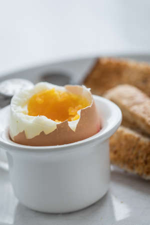Boiled brown egg with eggcup, salt shaker and toasted whole grain toast bread for breakfastの写真素材