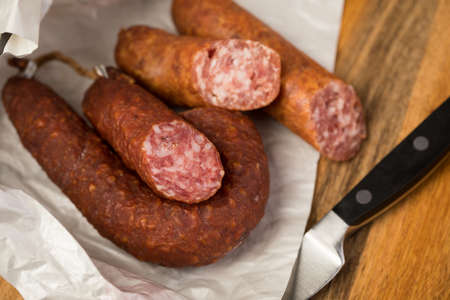 Ring salami pork sausage with German beer loaf in wax paper with wooden knife on wooden board background for lunch timeの写真素材