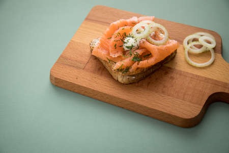 Smoked salmon on whole grain toast with onion rings, dill and horseradish on wooden boardの写真素材