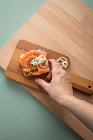 Woman eating smoked salmon on whole grain toast with onion rings, dill and horseradish of wooden boardの写真素材