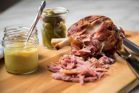 Grilled pork knuckle meat on wooden cutting board with pickled gherkins, sweet and medium hot mustard on marble backgroundの写真素材