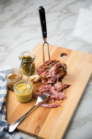 Grilled pork knuckle meat on wooden cutting board with pickled gherkins, sweet and medium hot mustard on marble backgroundの写真素材