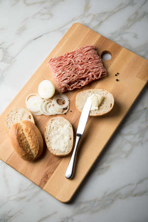 German snack bread roll buns with raw minced pork meat, butter, pepper and onion rings on wooden...