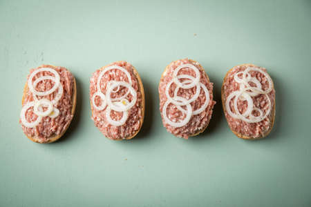 German snack bread roll buns with raw minced pork meat, butter, pepper and onion rings on mint green...