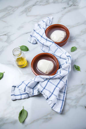 Mozzarella cheese balls, basil and olive oil on marble background with kitchen towelの写真素材