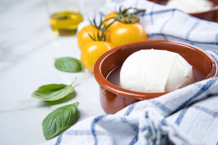 Yellow tomatoes with mozzarella cheese, basil and olive oil on marble background and kitchen towel
