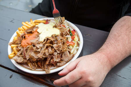 Man eating German DÃ¶ner Kebab dish with veal, salad, French fries hot sauce and herb sauceの写真素材