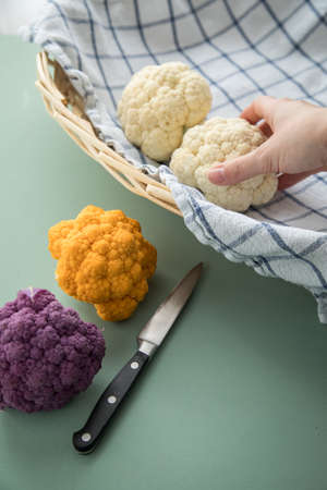 Colorful rainbow cauliflower in purple, orange and white on kitchen towel with knife in basket on...