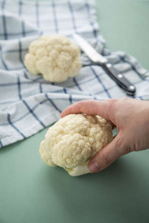 Woman cooking white cauliflower on kitchen towel with knife on pastel green backgroundの写真素材