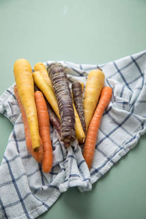 Colorful rainbow carrots in purple, orange and yellow on kitchen towel on pastel mint green backgroundの写真素材