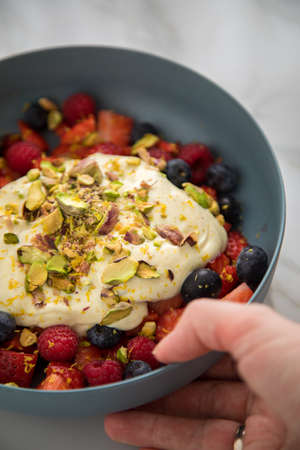 Woman eating berry fruit salad with strawberries, blueberries, raspberry, pistachio, lemon zest and...