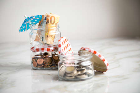 3 glass jars with Euro notes, sunshade, 2â¬ coins and loose cash for housekeeping and vacation savingsの写真素材