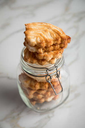 Italian puff pastry fan wavers cookies biscuits with preserving glass jar on marble table backgroundの写真素材